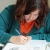 Photo of a white woman with brown hair, wearing a teal cardigan over an orange shirt, drawing.