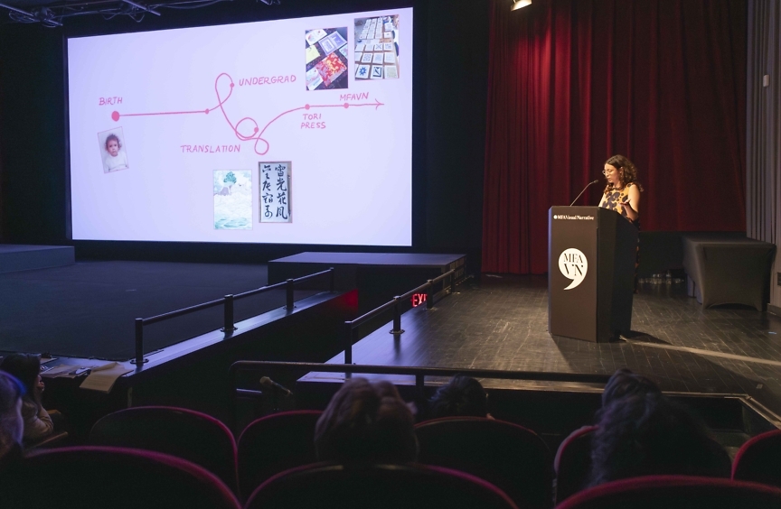 A student of the MFA Visual Nararative Program at SVA stands at the podium of a theatre. To her left, a large projector screen shows her presentation, with a slide illustrating her journey to the program.