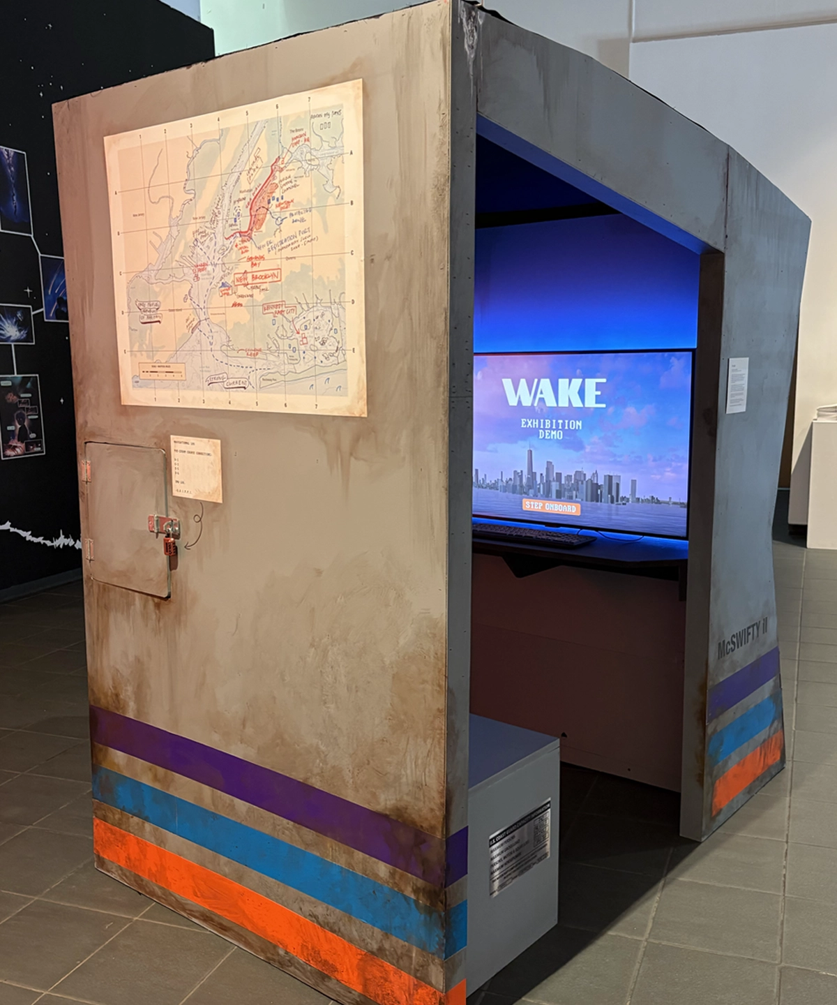 The back of a large grey booth which depicts a map of NYC Waterways and a compartment padlocked shut with a small note pointing to the lock.